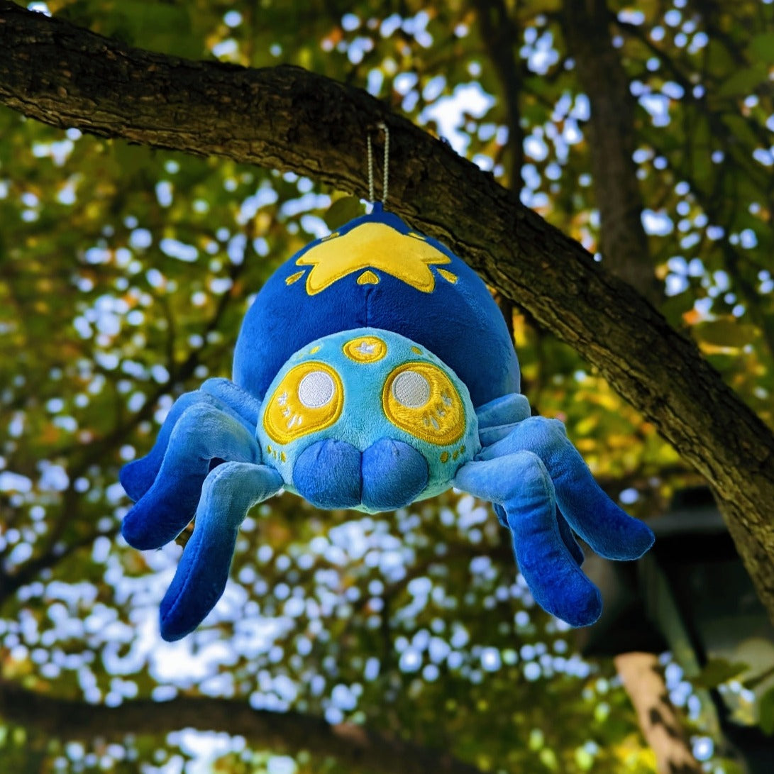 A photograph of a tree with a plush spider on it. The spider's name is Cosmo. They are blue with yellow eyes and a yellow star on it's butt.