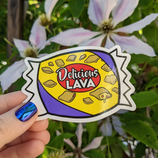 A photograph of a vinyl sticker being held in front of a clematis plant. The vinyl sticker is of a bag of pizza rolls that says, “Delicious lava.”