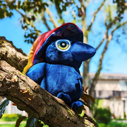 A photograph of a plush toy Raven in a tree on a sunny day.