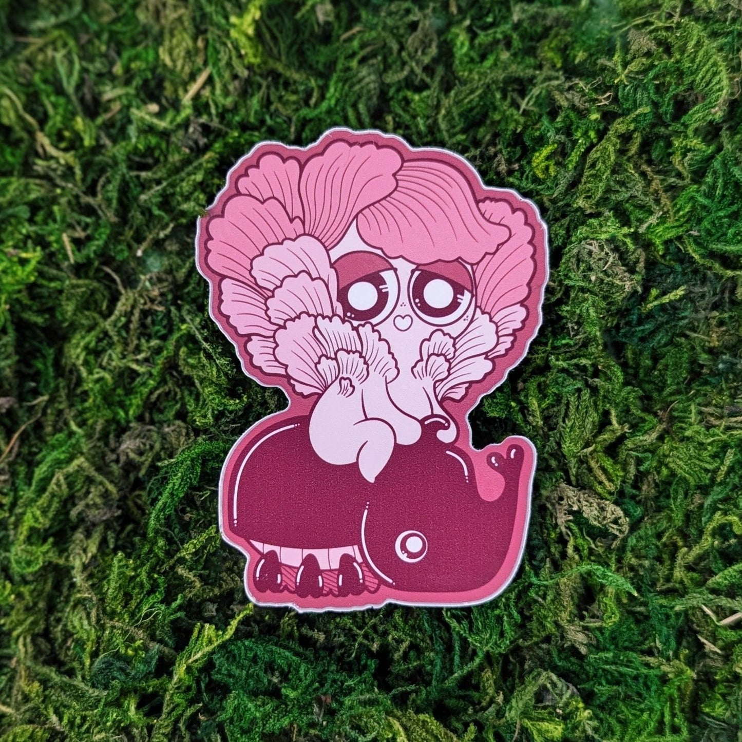 Photograph of a mossy background with a vinyl sticker of a pink oyster Mushkinriding on a pink beetle.