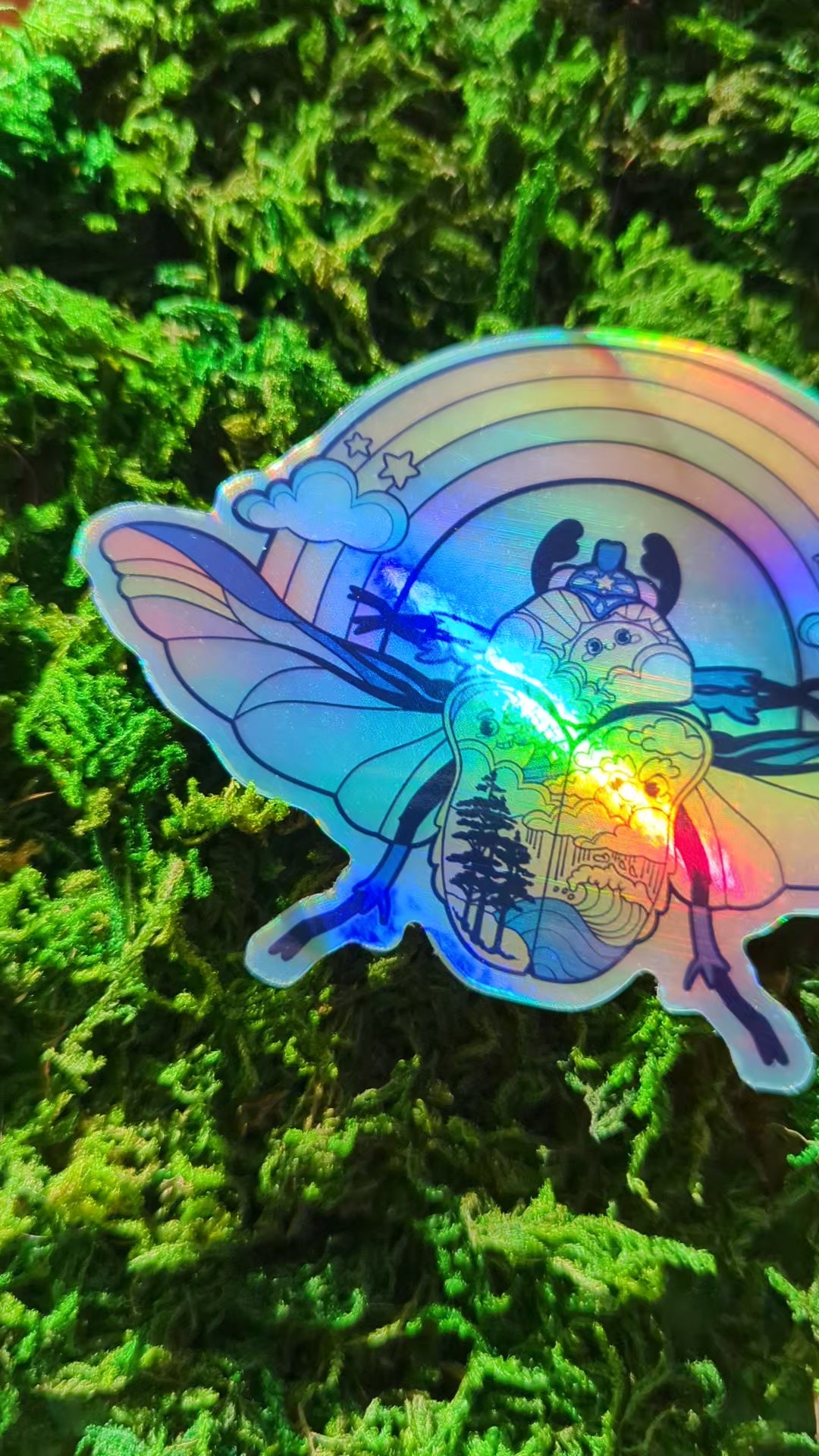 Video of a mossy background with a holographic vinyl sticker a beetle with a land and sea theme. The video shows how shiny the holographic effect is.