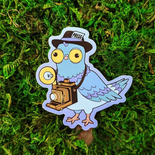 Photograph of a mossy background with a vinyl sticker of a pigeon dressed as a journalist photographer.