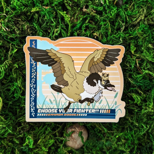 Photograph of a mossy background with a vinyl sticker of a Canada Goose with a cardboard crown and a kitchen knife. Under the goose it says, “Choose your Fighter!!! Canada Goose”
