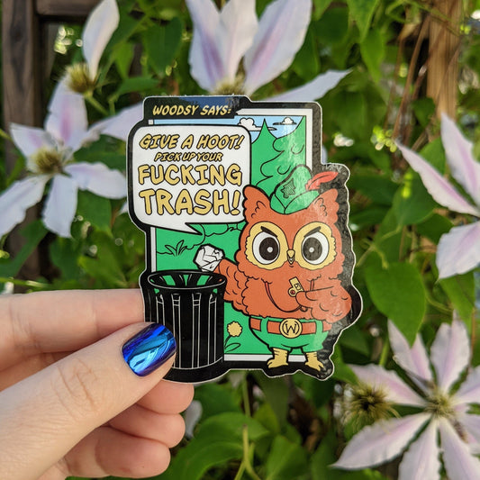 A photograph of a vinyl sticker being held in front of a clematis plant. The sticker is of Woodsy the owl with a whistle putting a piece of trash into a garbage can. Woodsy is saying: “Give a hoot! Pick up your fucking trash!”