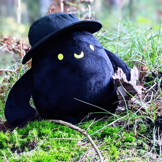 Photograph of Mr. Hat Plush hanging out in some moss and foliage.