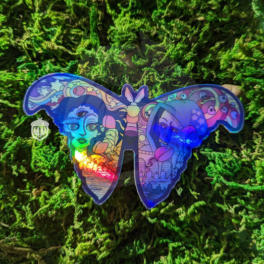 A photograph of a vinyl sticker being held in front of a clematis plant. The vinyl sticker is of a holographic moth. One wing has the representation of life and one has death and they’re both speaking on the phone.