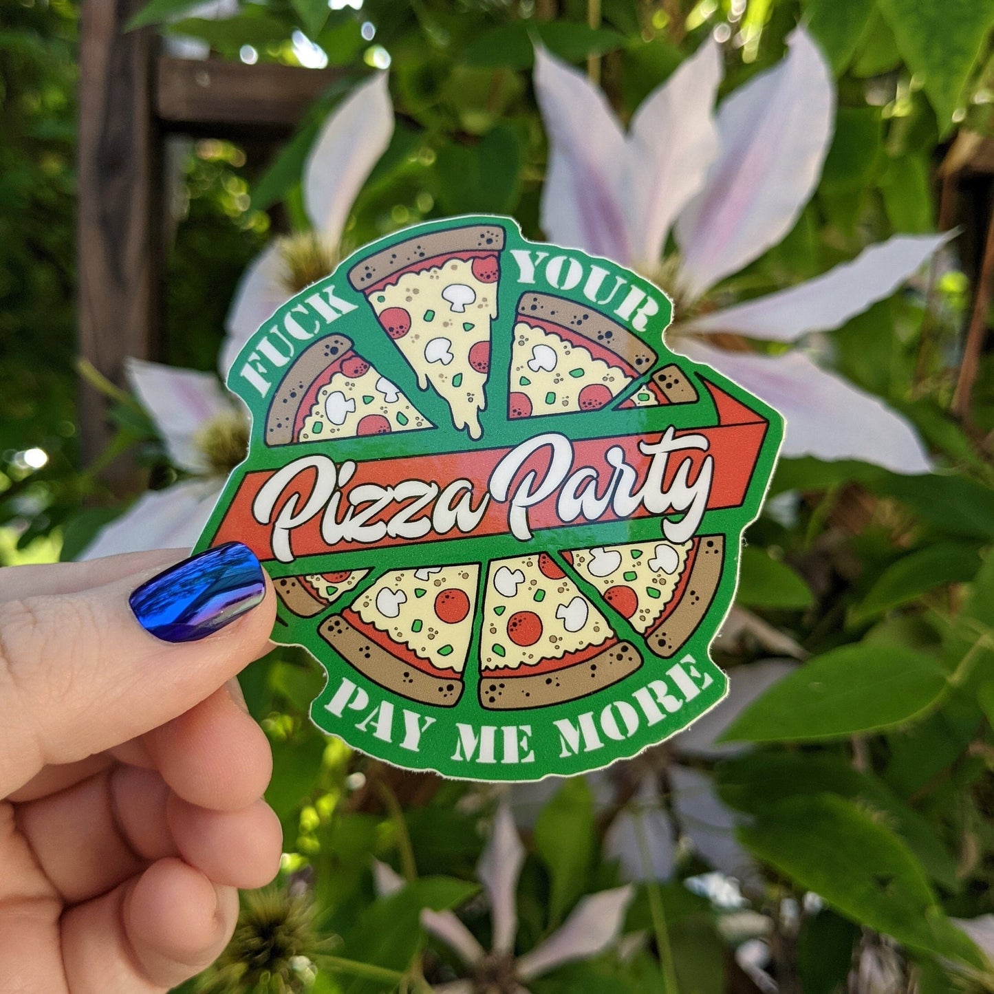 A photograph of a vinyl sticker being held in front of a clematis plant. The vinyl sticker is a pizza with a banner around it that says, “Fuck your pizza party, pay me more!”