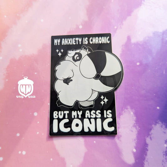 A photograph of a vinyl sticker against a pink and purple background. The sticker features Chaps the Raccoon standing with his little booty out. Around him it says, “My anxiety is chronic but my ass is iconic.”