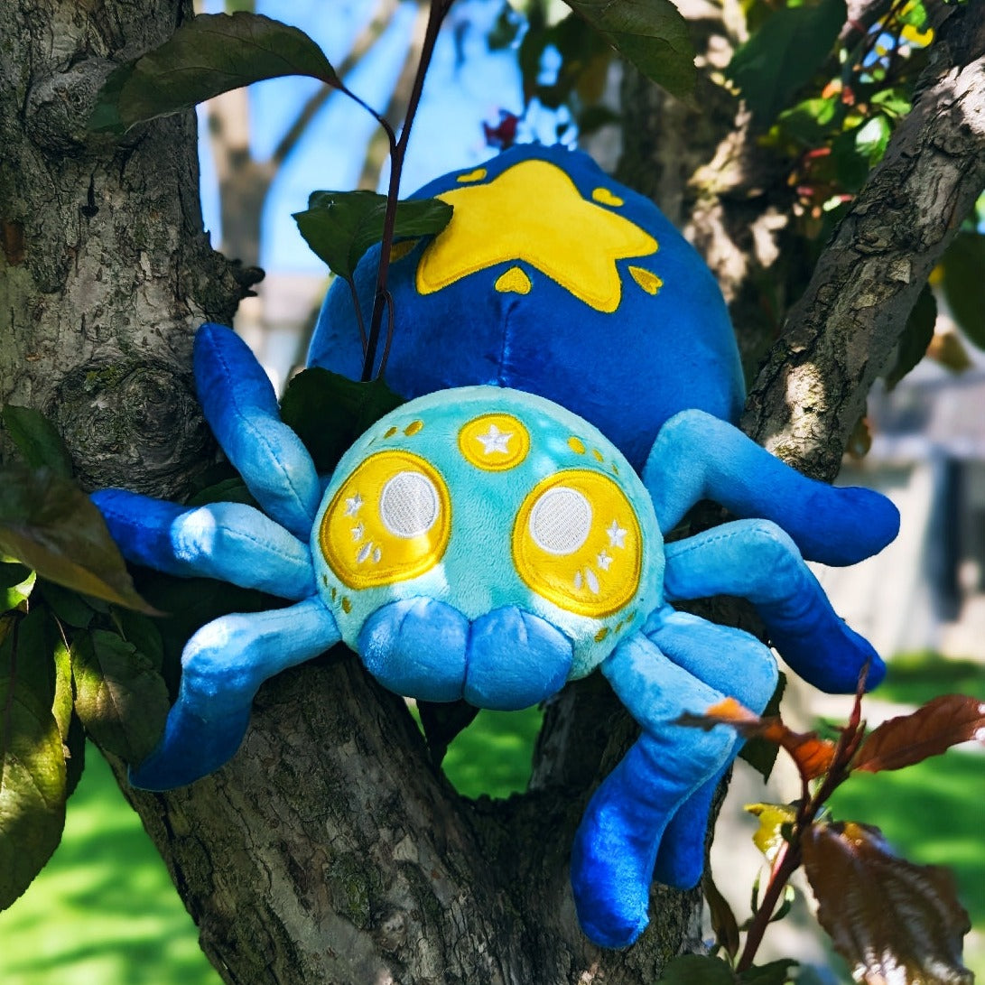 A photograph of a tree with a plush spider on it. The spider's name is Cosmo. They are blue with yellow eyes and a yellow star on it's butt.