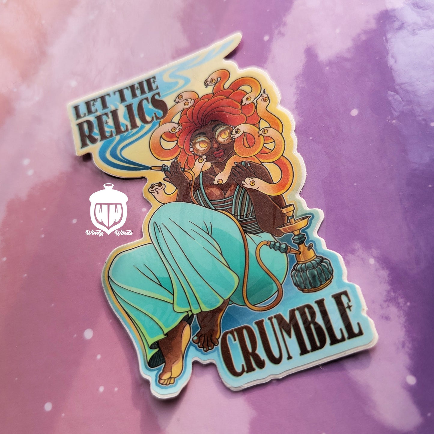 A photograph of a vinyl sticker against a pink and purple background. The sticker features Medusa lounging and smoking hookah. Around her it says, “Let the relics crumble.”