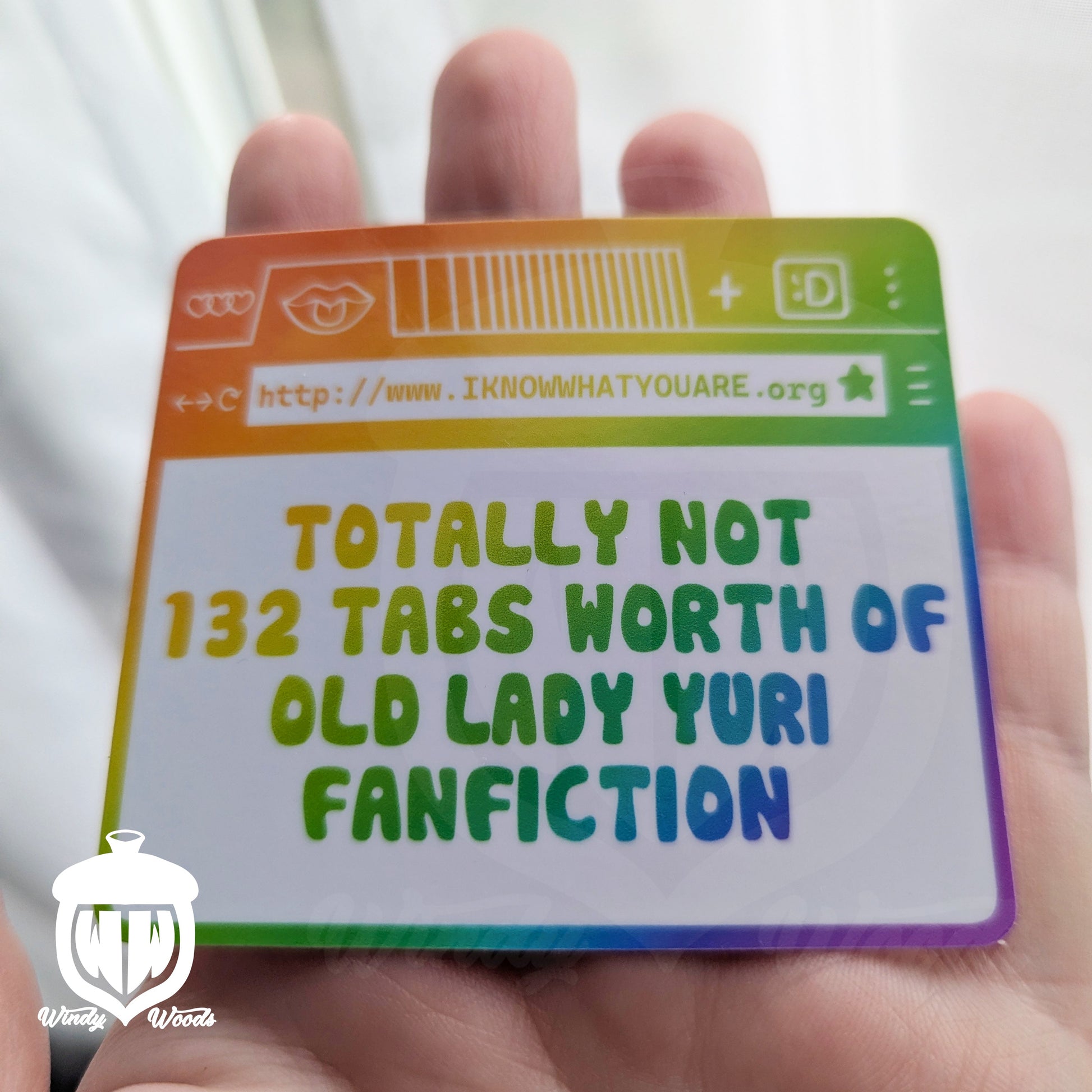 A photograph of a vinyl sticker being held in an outstretched hand. The sticker shows an internet browser in rainbow colors. The page says, "Totally Not 132 tabs worth of old lady yuri fanfiction" and the website above it says, "WWW.Iknowwhatyouare.org"