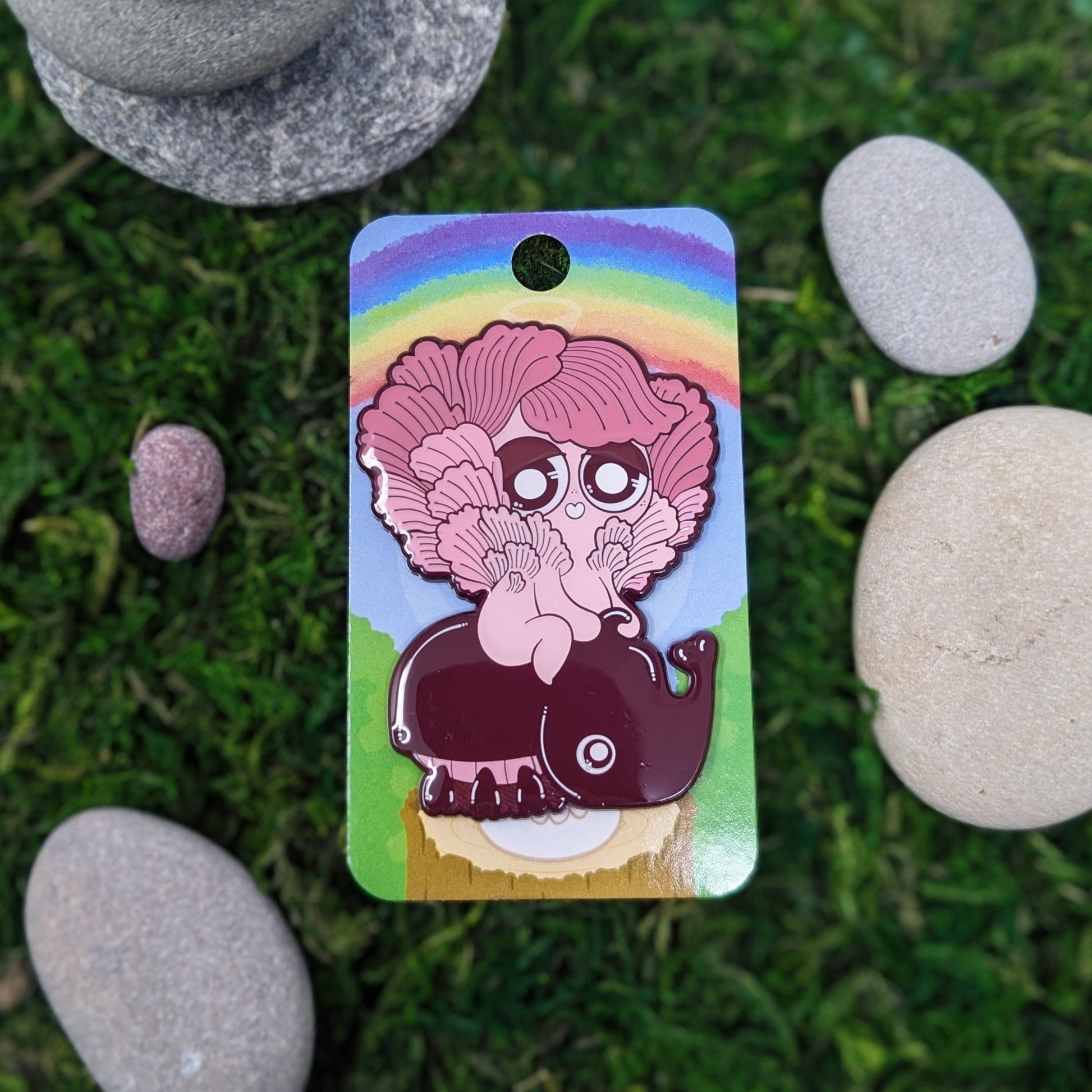 Photograph of a mossy background with an enamel pin of a Pink Oyster Mushroom Sprite called a Mushkin. The Mushkin is riding on a big pink beetle.