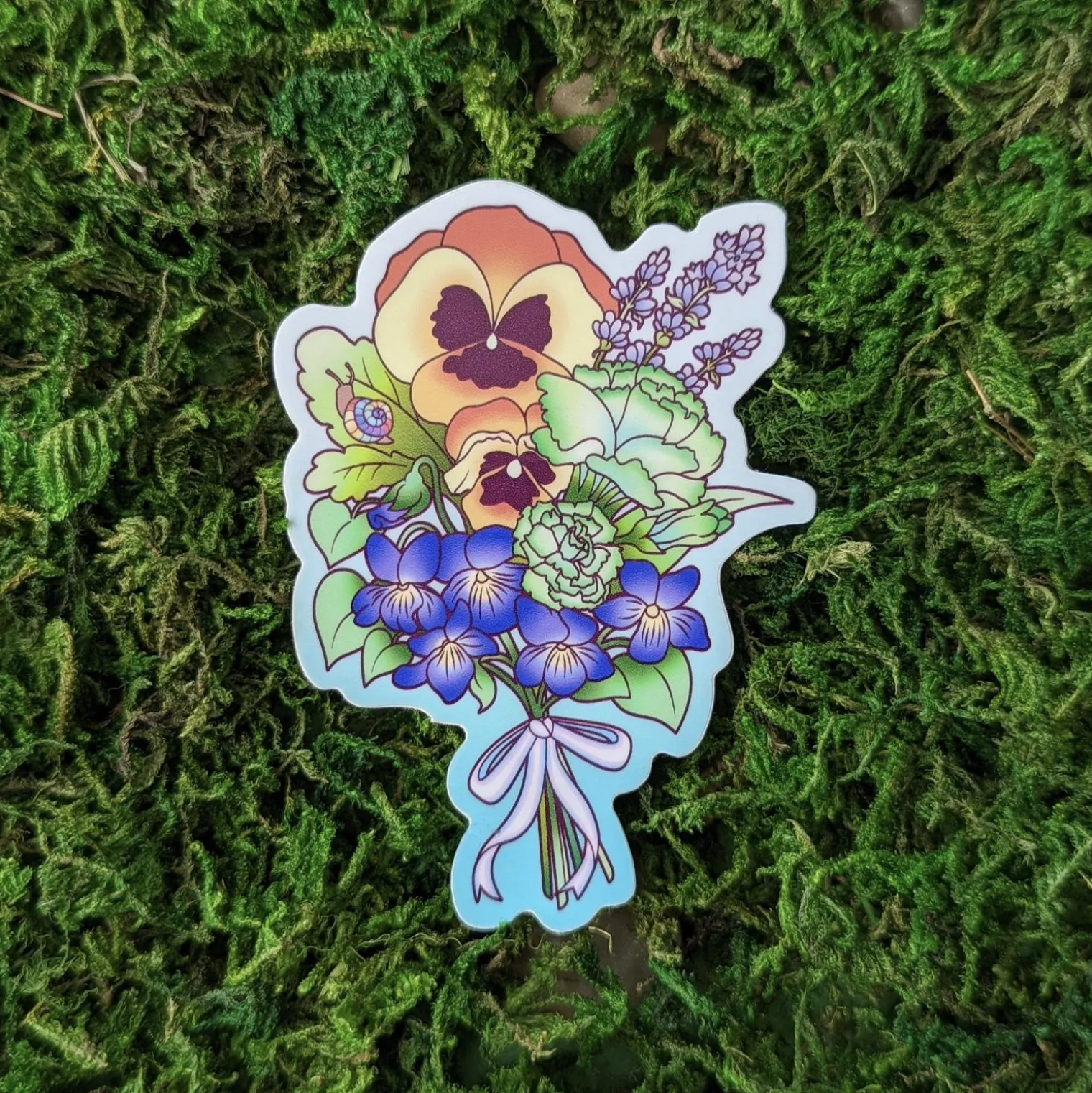 Photograph of a mossy background with a vinyl sticker of a flower bouquet featuring queer themes.