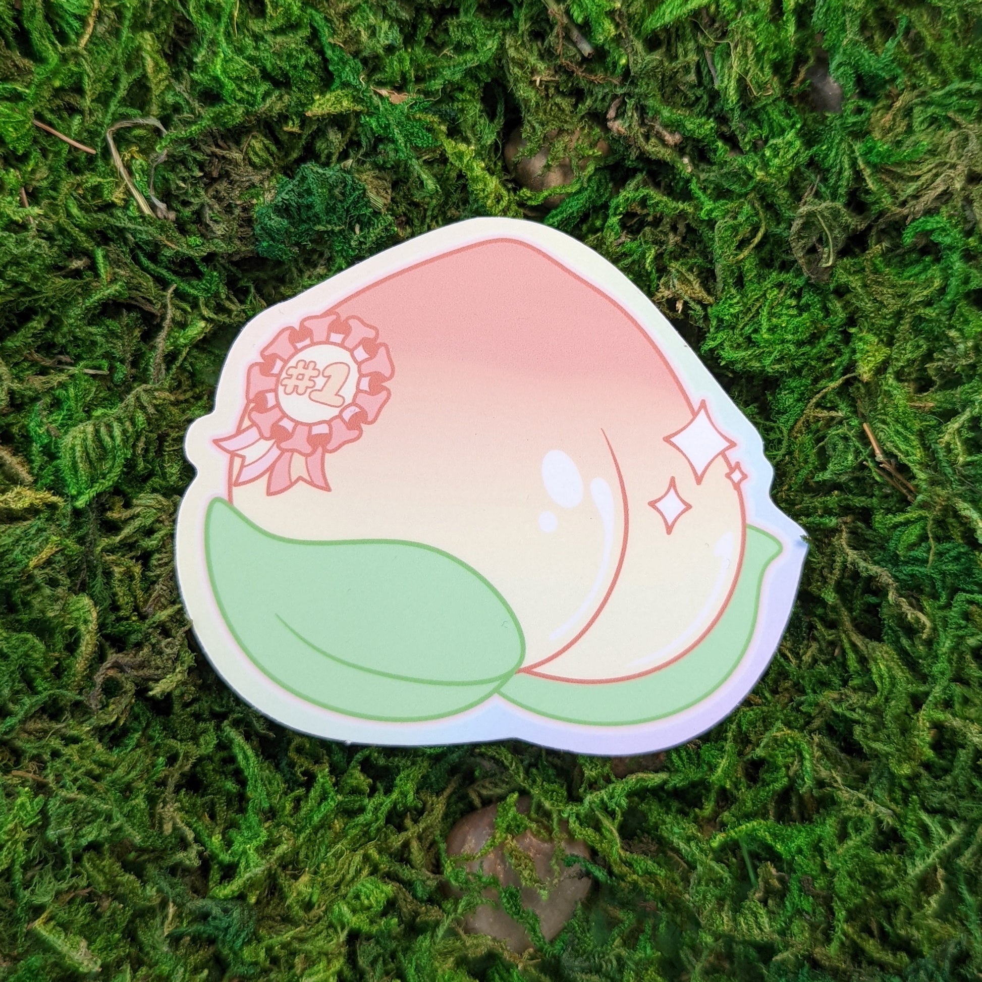 Photograph of a mossy background with a 3 inch vinyl sticker of a shiny peach with a sparkly #1 ribbon on it.