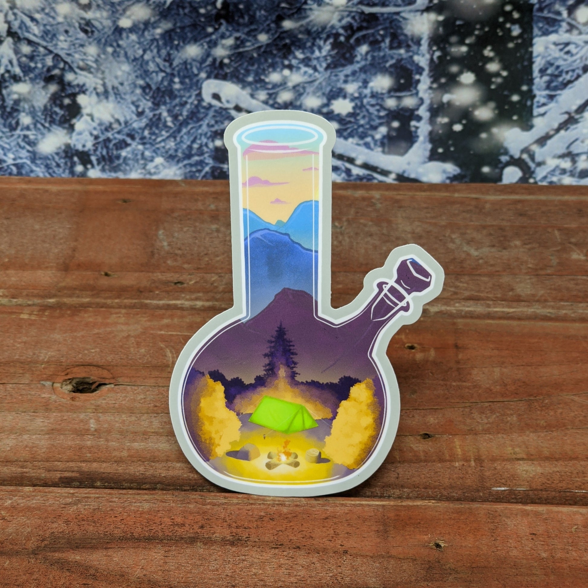A redwood background with a snowy backdrop. On the wood is a vinyl sticker of a bong with a sunset camping scene within it.