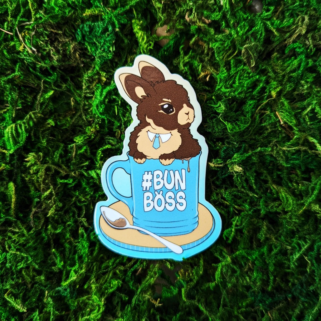 Photograph of a mossy background with a vinyl sticker of a brown rabbit in a coffee cup that says #BUNBOSS