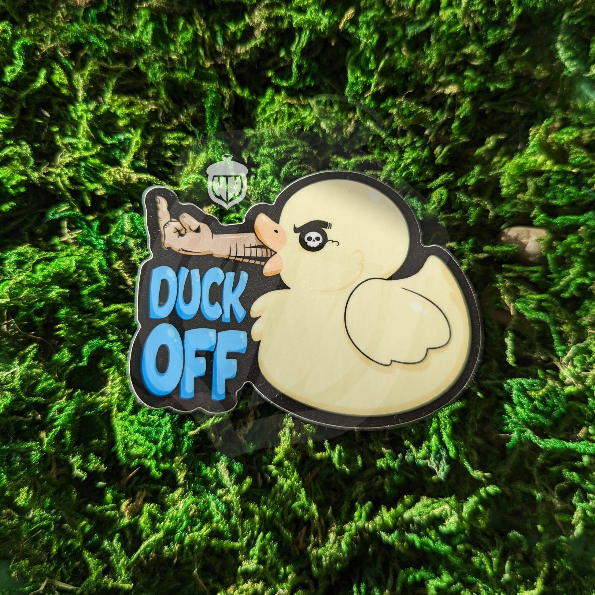 Photograph of a mossy background with a vinyl sticker of a duck with a human arm flipping the middle finger. Under the middle finger it says “Duck off”