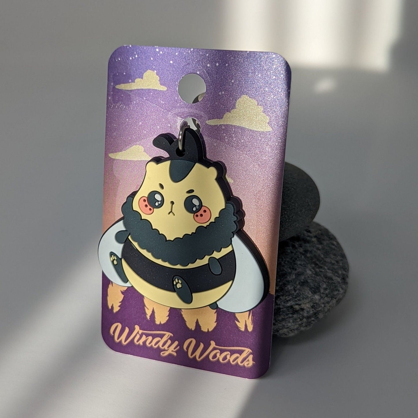 A PVC Keychain of a hamster bumble bee hybrid creature called a Honeyham leaning against some rocks on a packaging card that says Windy Woods.