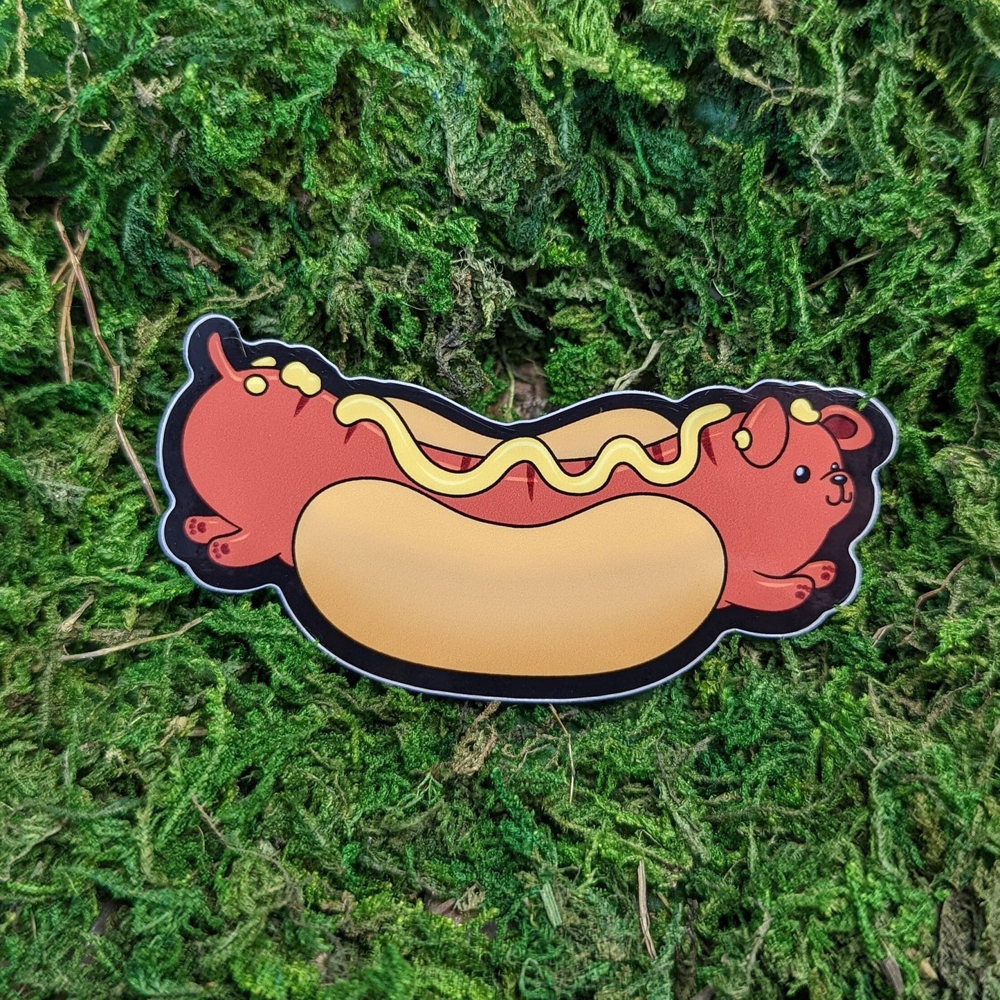 Photograph of a mossy background with a vinyl sticker of a hot dog themed dog.