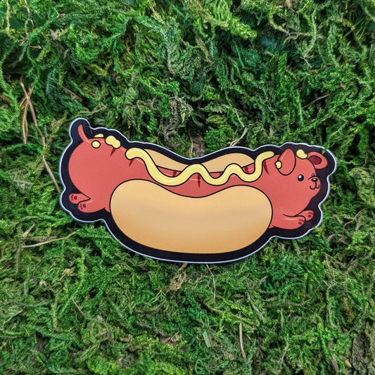 Photograph of a mossy background with a vinyl sticker of a hot dog themed dog.