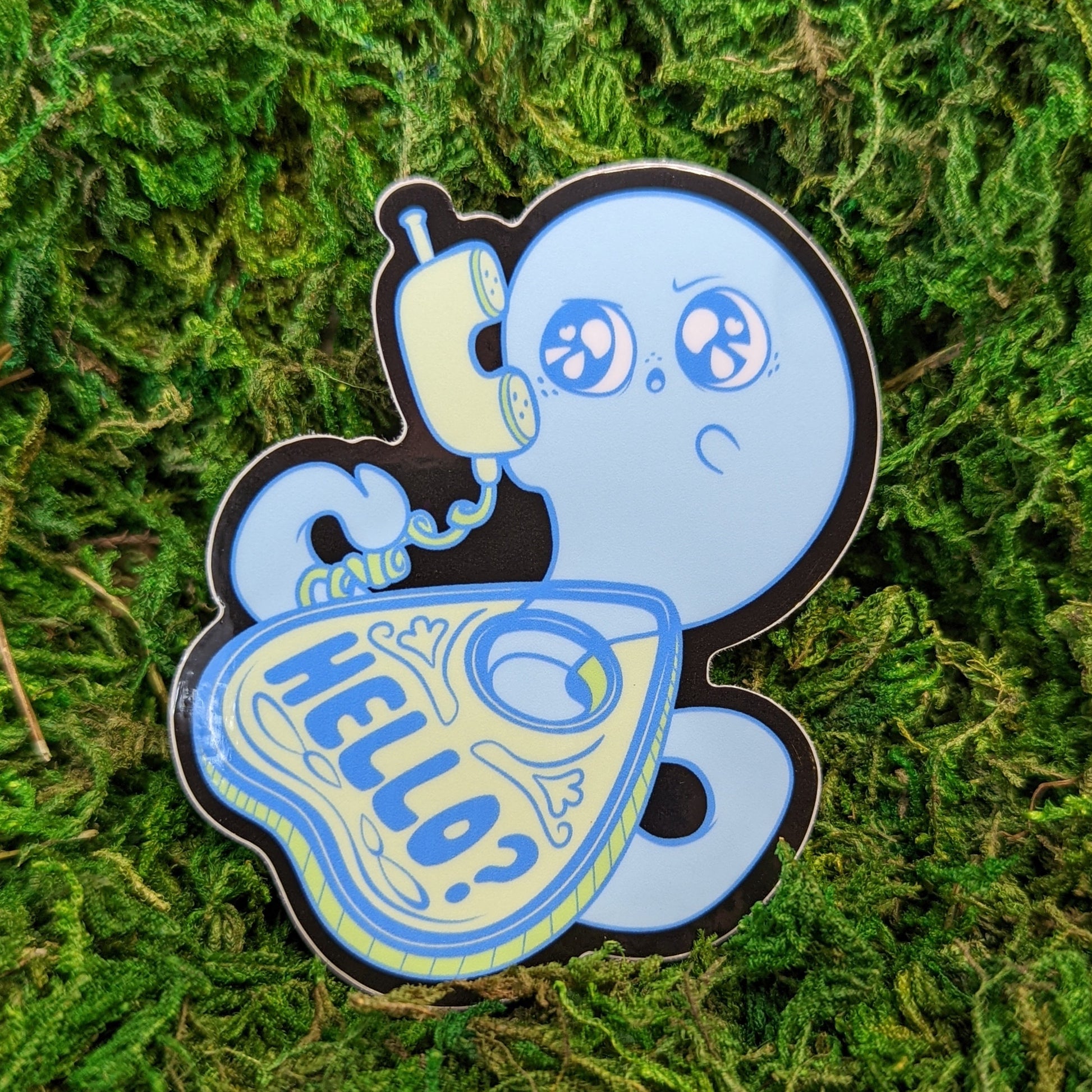 Photograph of a mossy background with a vinyl sticker of a ghost coming out of a planchette and answering a corded phone saying, “Hello?”