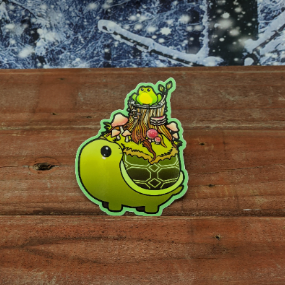 A redwood background with a snowy backdrop. On the wood is a vinyl sticker of a green turtle with a marshy tree stump covered in mushrooms and a frog.