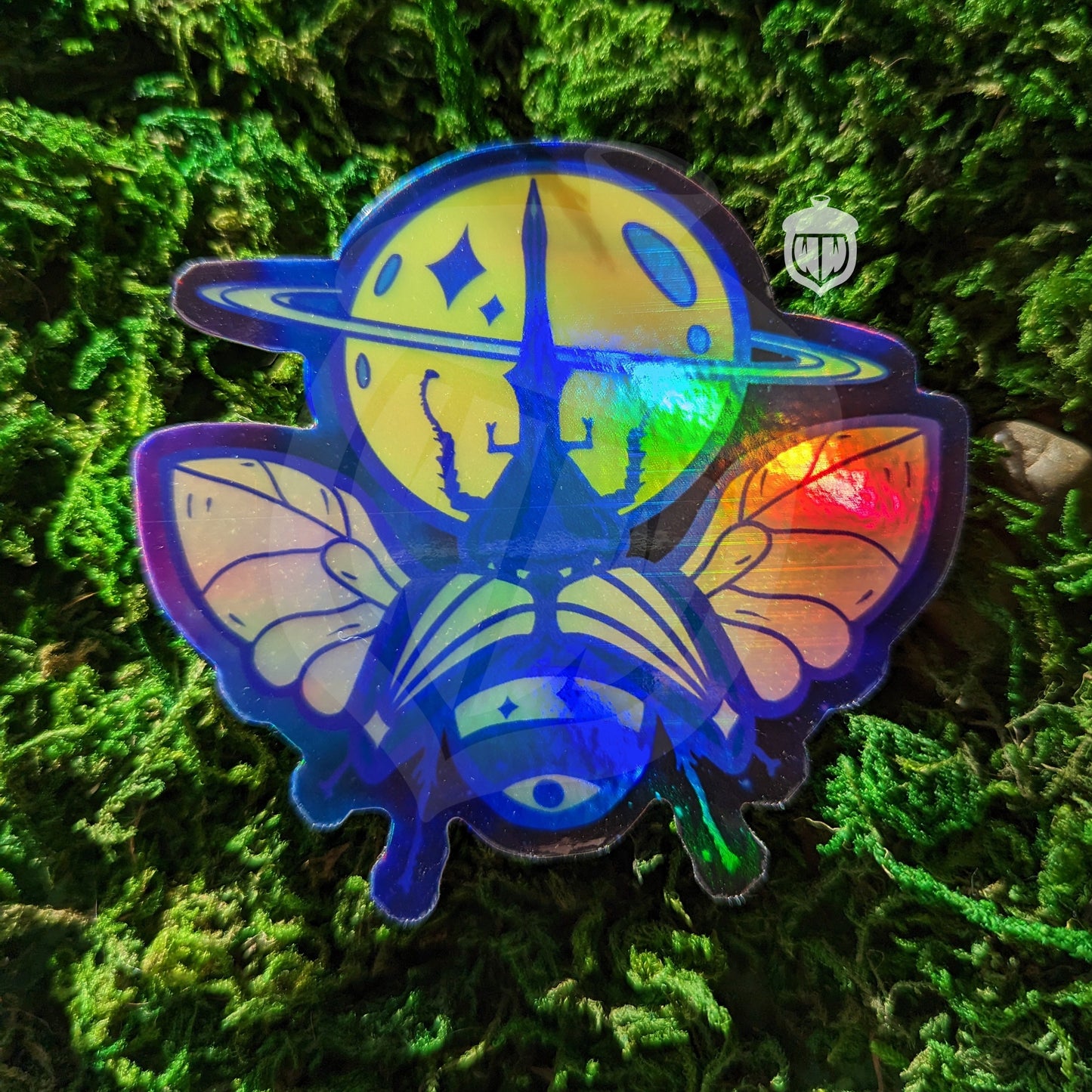 Photograph of a mossy background with a holographic vinyl sticker a hercules beetle with a saturn theme.