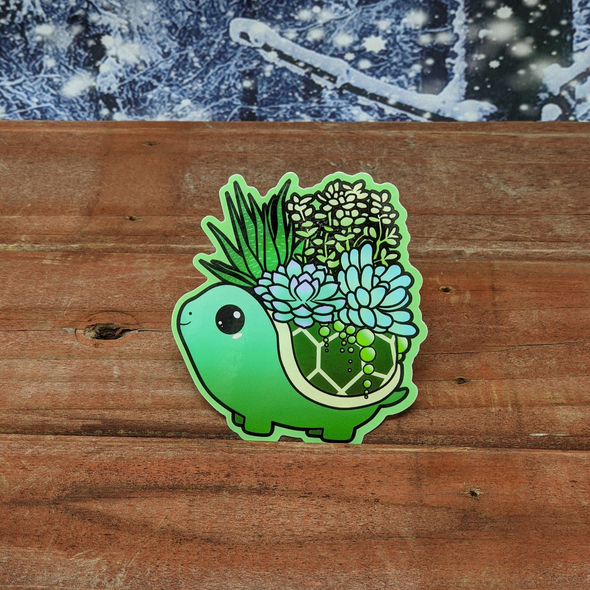 A redwood background with a snowy backdrop. On the wood is a vinyl sticker of a green turtle with succulents growing out of its shell.