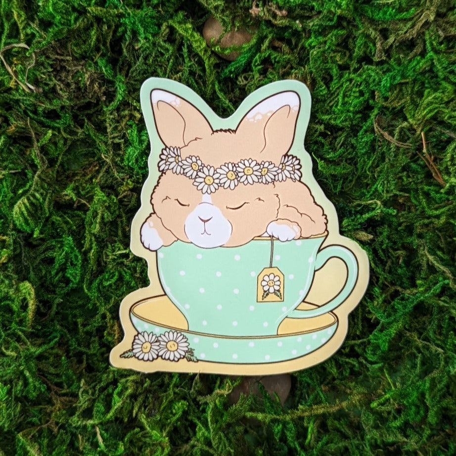 Photograph of a mossy background with a vinyl sticker of a tan rabbit in a tea cup with a flower crown.